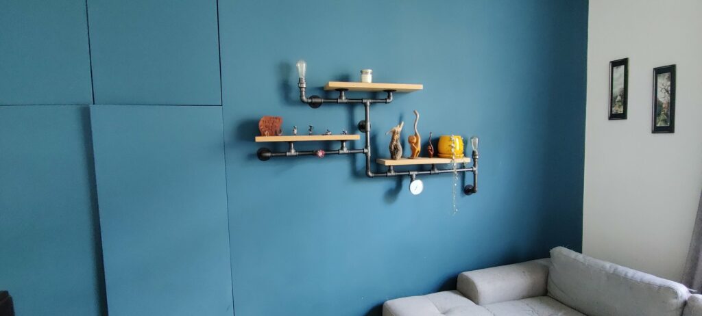 L'étagère steampunk sur le mur bleu, la vanne rouge sur le tuyau du bas